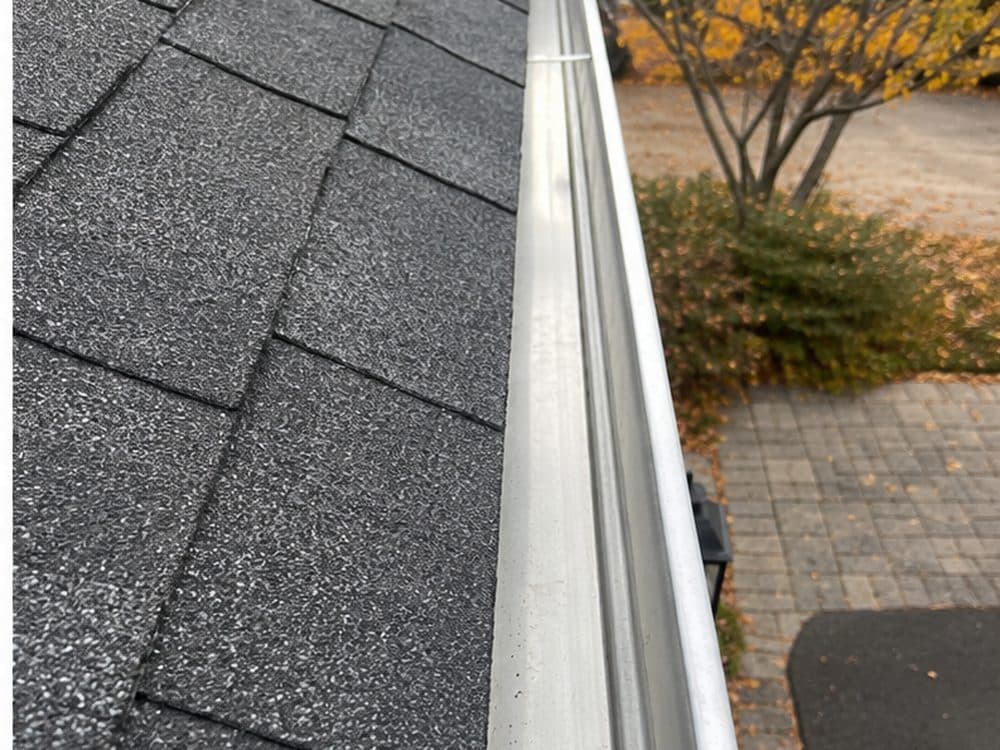 A clean aluminum gutter along a shingle roof edge after a Vent Pro cleaning