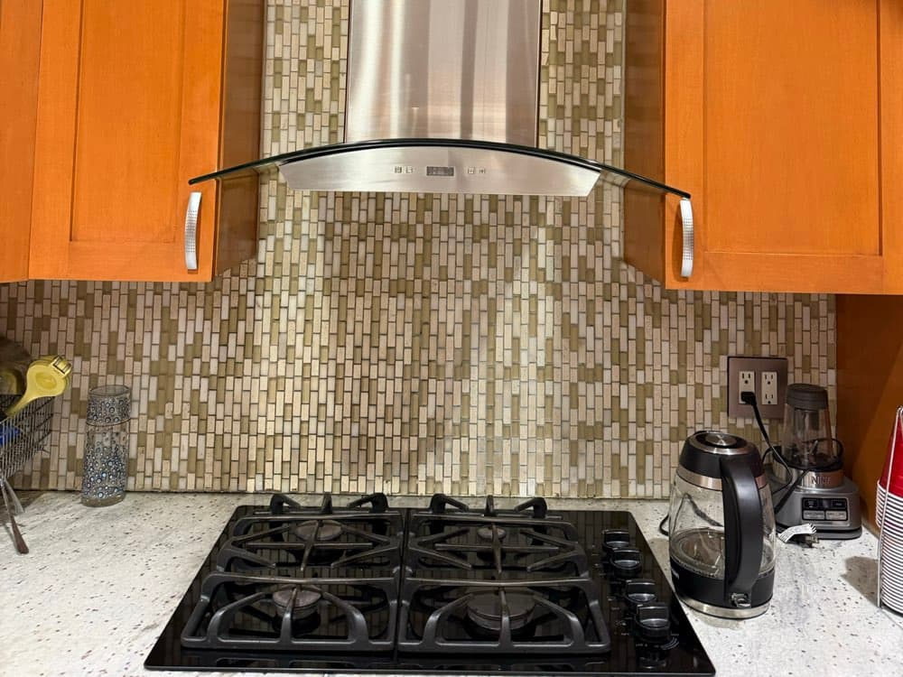 A stainless steel range hood with a glass canopy over a gas cooktop in a Brooklyn kitchen